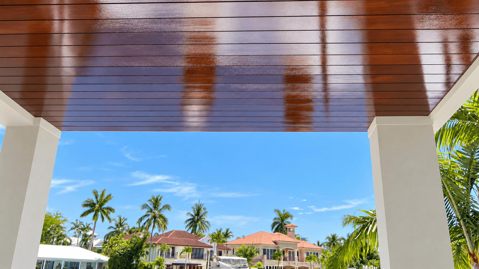 Stained wood porch ceiling framing a view of waterfront homes and palm trees in South Florida
